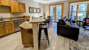 A spacious living area with a kitchen, wooden cabinets, a large window, and a black leather sofa. - Trappers Crossing 8769 (Keystone)