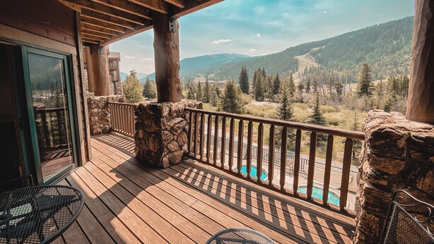 Un terrazzo in legno con un muro in pietra, una piscina e vista sulle montagne.