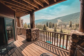 A wooden deck with a stone wall, a pool, and a mountain view. - Hidden River Lodge 5965 (Keystone)
