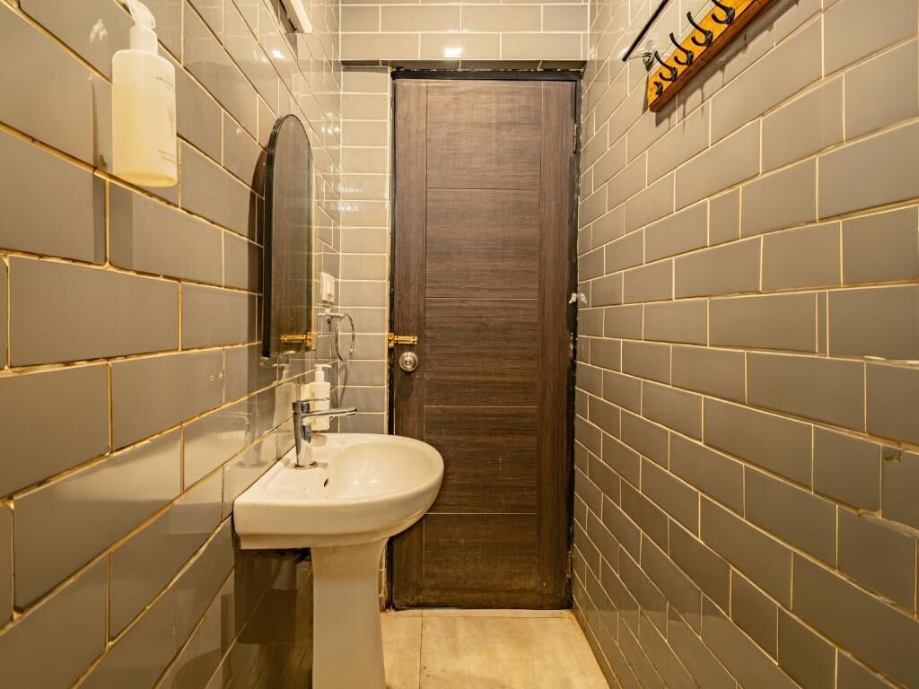 Bany estret amb una porta de fusta, un lavabo blanc i un mirall.