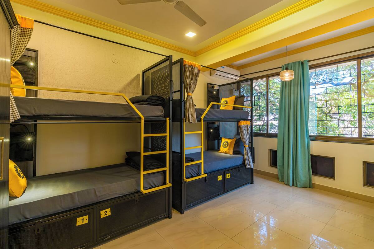 A dormitory room with bunk beds, a ceiling fan, and a window with curtains.