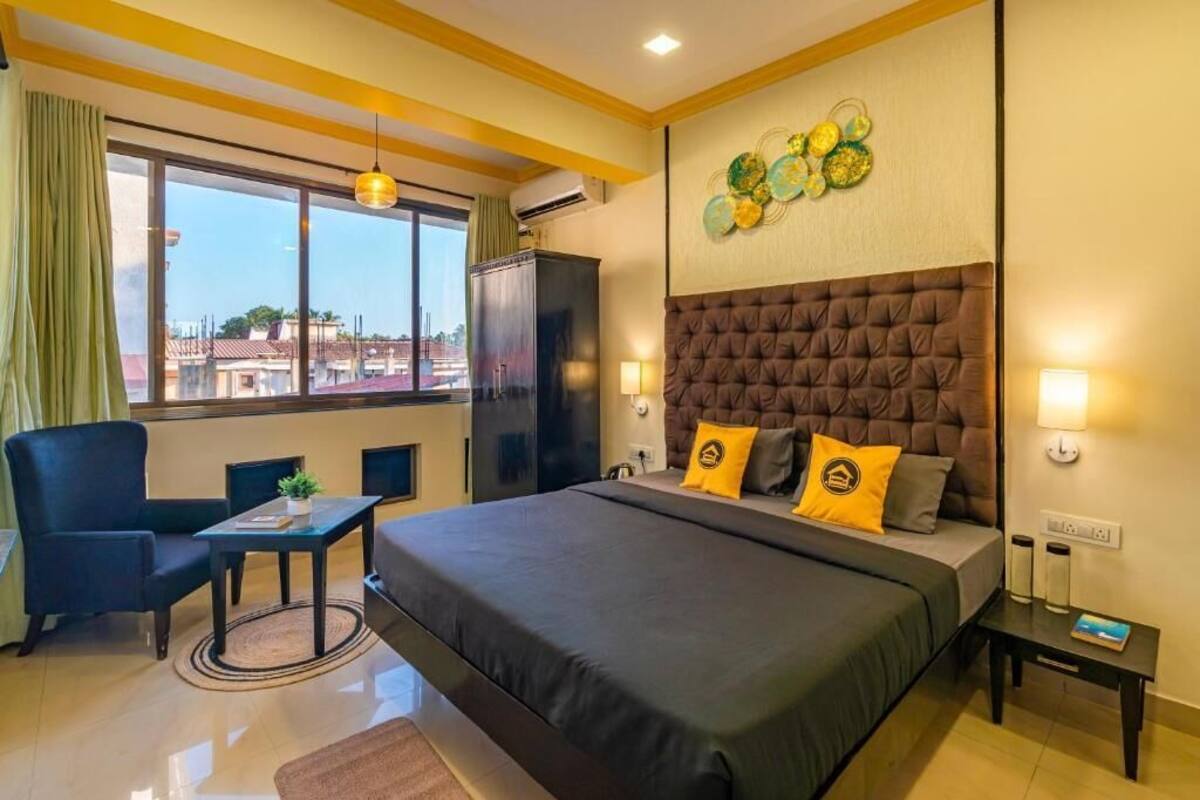A hotel room with a large bed, a desk, a chair, and a view of the city through large windows.