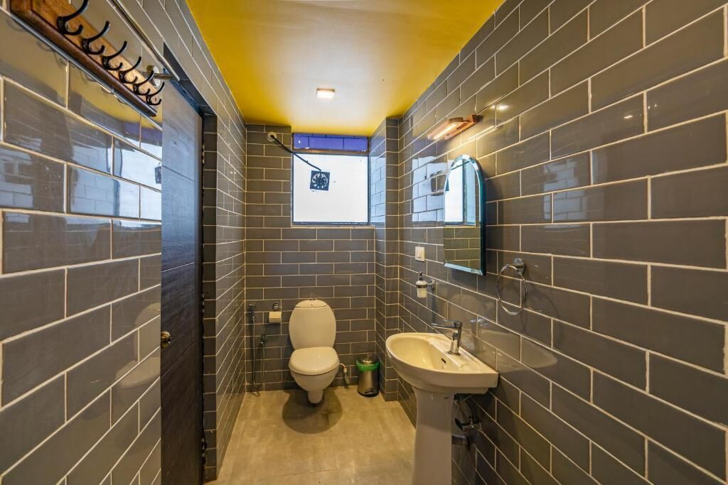 A compact bathroom with dark tiled walls, a white toilet, a sink, and a small window.