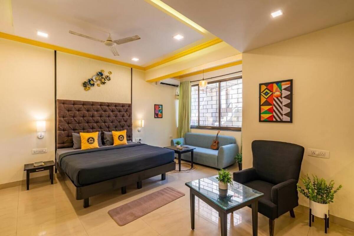 A modern hotel room with a large bed, a sofa, a chair, a small table, and a window with curtains.