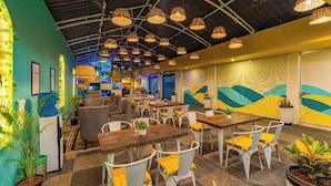 A restaurant with a high ceiling, hanging wicker lamps, and a mural on the wall.