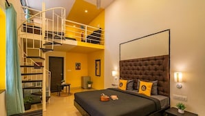 A bedroom with a large bed, a headboard, two bedside tables, a small desk, a chair, a staircase, and a door.