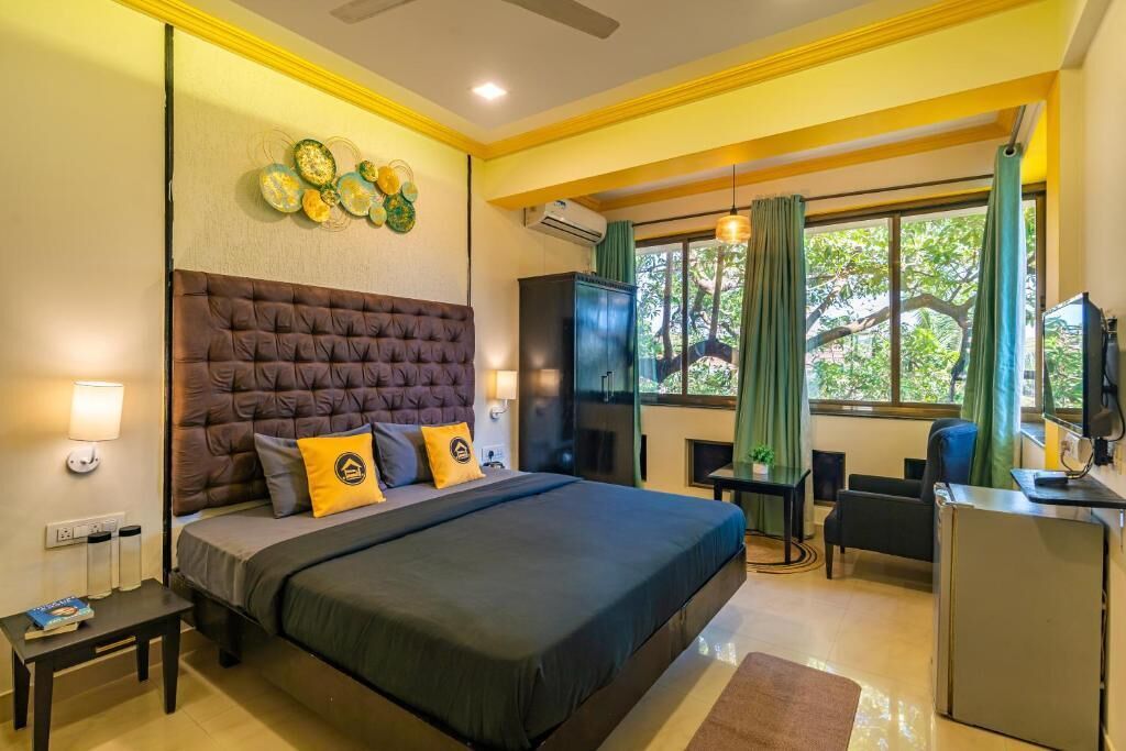 Quarto de hotel com uma cama grande, uma escrivaninha, uma TV e uma janela com cortinas.