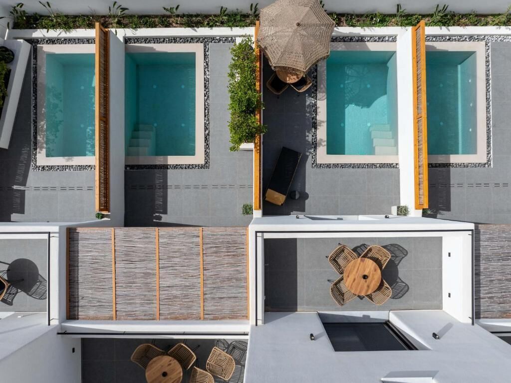 A modern hotel with three separate pools, each with a lounge chair and umbrella.