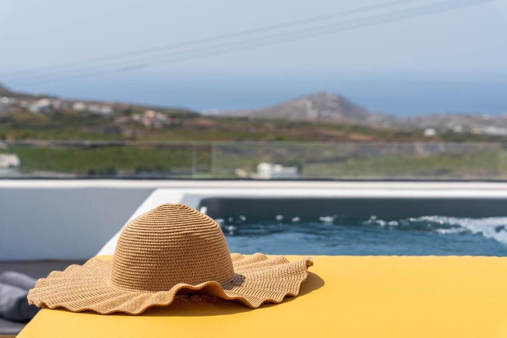 A straw hat on a yellow surface with a view of the sea and a distant hill.