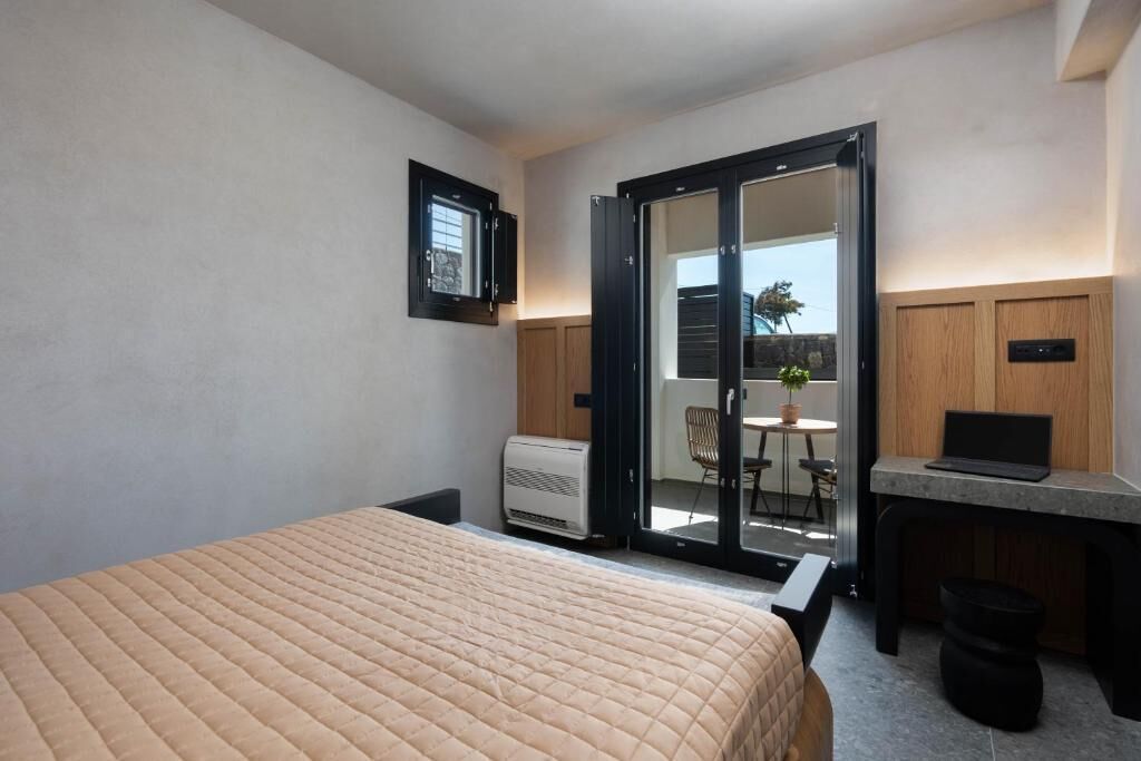 Une chambre d’hôtel comprenant un lit, un bureau avec un ordinateur portable, une petite table avec une chaise et une porte coulissante donnant sur un espace extérieur.