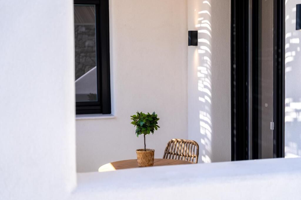 Un petit espace extérieur aménagé avec une table, une chaise en osier et un pot de fleurs.