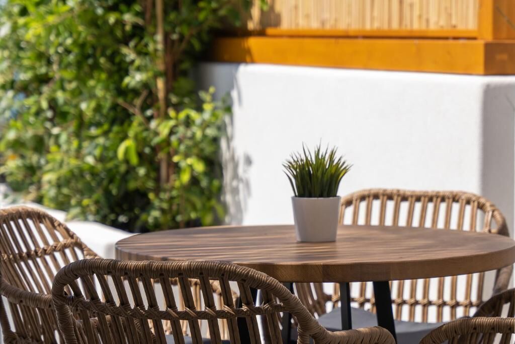 Een ronde houten tafel met een potplant, omringd door rieten stoelen.