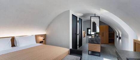 Une chambre à coucher moderne avec un lit, un banc et un coin cuisine équipé de placards et d’un plan de travail.