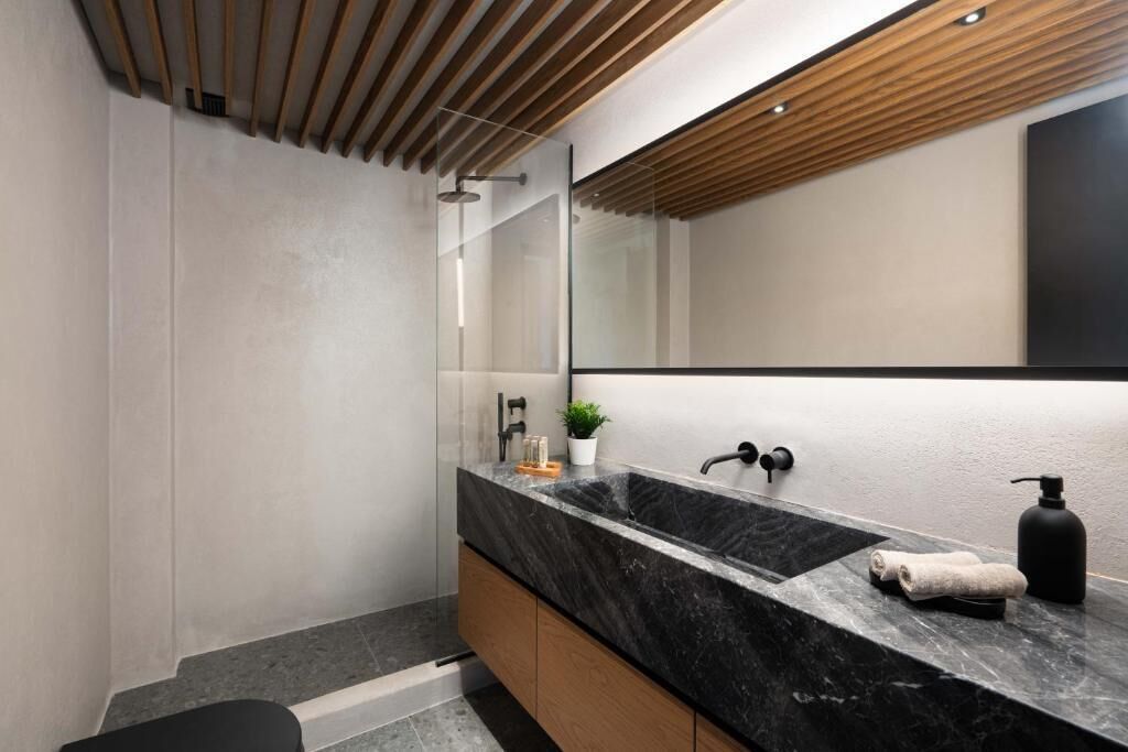 Un baño moderno con un lavabo de mármol negro, armarios de madera y un espejo grande.