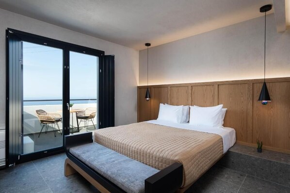 Un dormitorio moderno con una cama grande, un banco y una puerta corrediza de vidrio que da a un balcón con sillas.
