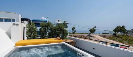 Un espace piscine aménagé sur le toit, avec un transat jaune, entouré de murs blancs et offrant une vue dégagée sur la mer.