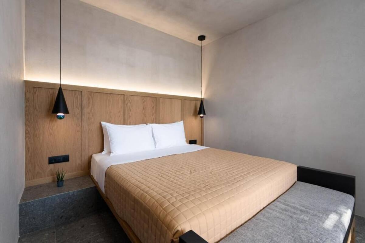 Ein modernes Hotelzimmer mit einem großen Bett, einem Holz-Kopfteil und zwei Pendelleuchten.
