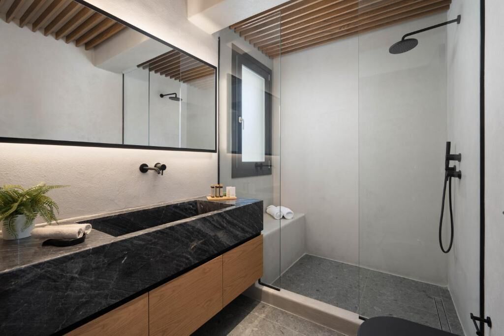 A modern bathroom with a black marble sink, wooden cabinets, a large mirror, and a glass-enclosed shower area.
