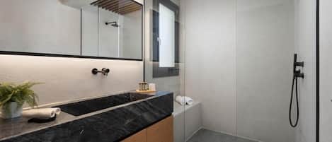 A modern bathroom with a black marble sink, wooden cabinets, a large mirror, and a glass-enclosed shower area.