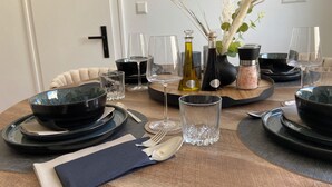 Ein Esstisch mit schwarzen Schüsseln, Tellern und Besteck, dazu klare Gläser und eine Vase mit Trockenblumen.