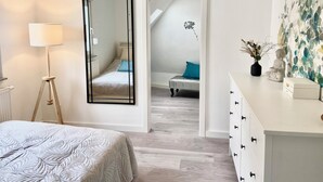 Ein Schlafzimmer mit einem Bett, einer Stehlampe, einem Spiegel, einer Kommode und einem Bild.