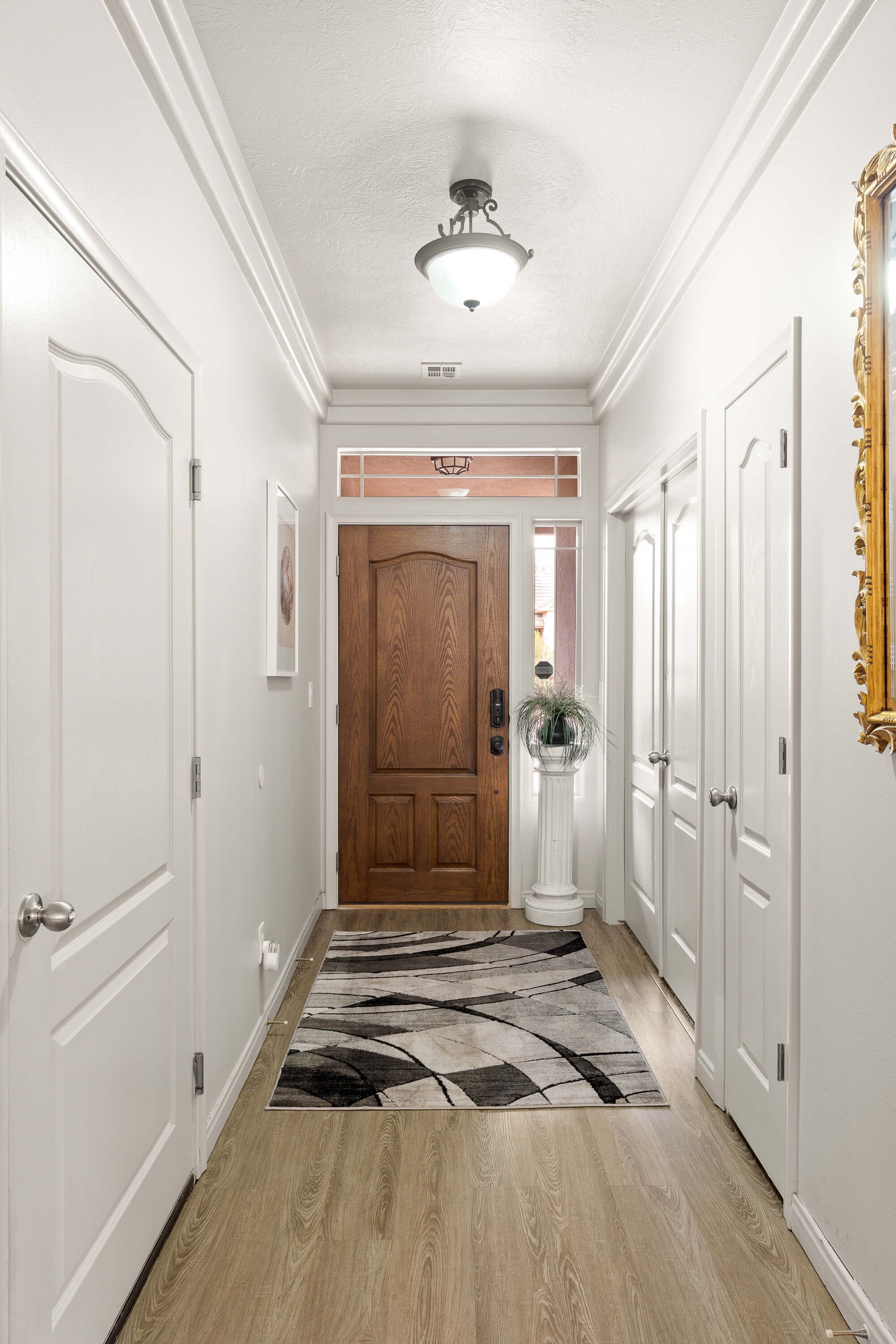 A hallway with white walls, a wooden door, and a patterned rug.