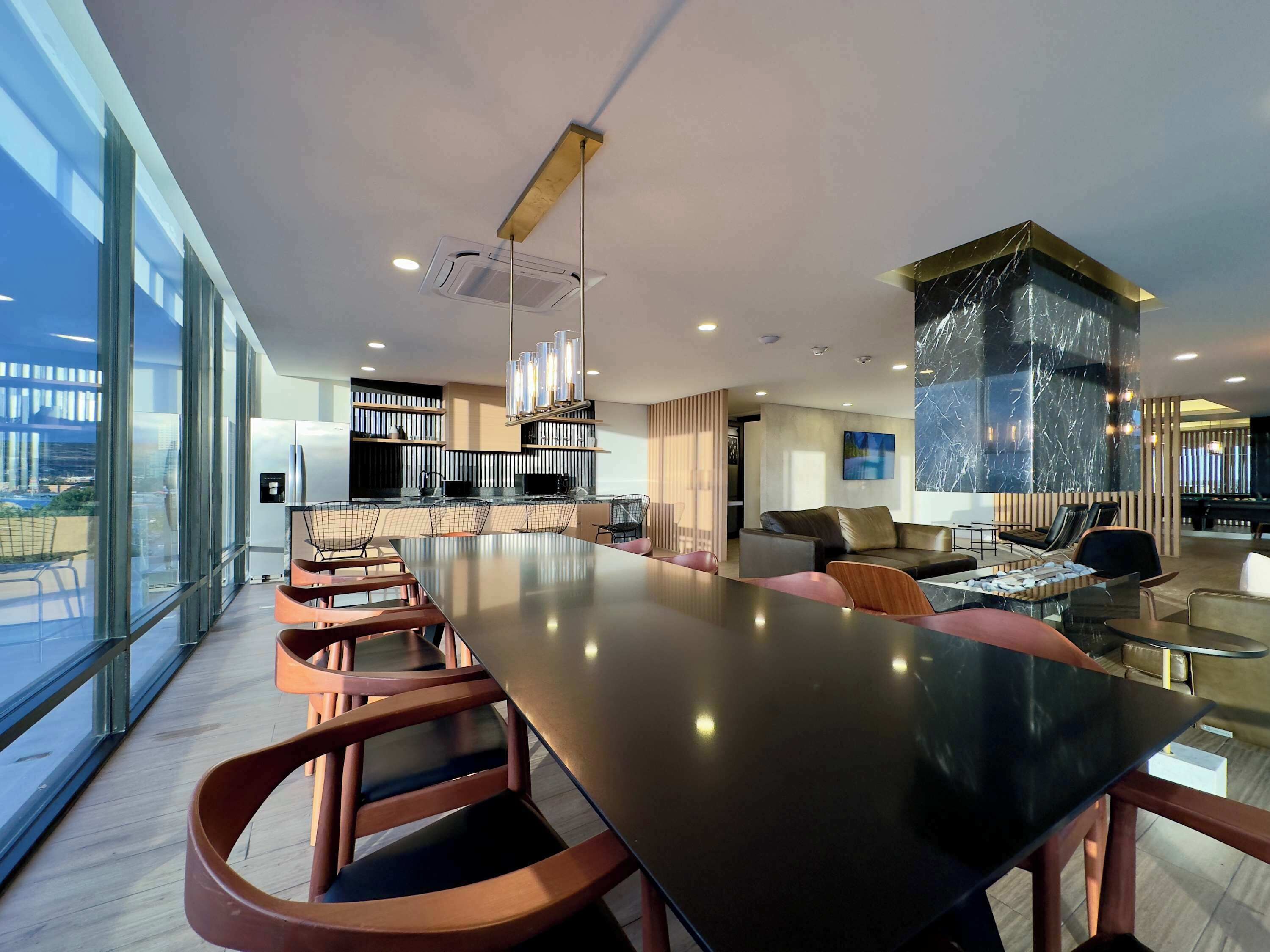 Een modern interieur met een lange eettafel, stoelen, een keukenhoek en een groot raam met uitzicht op de stad.