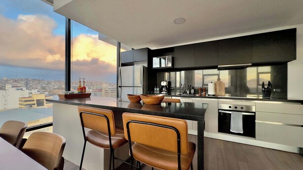 Una cocina moderna con una isla grande, taburetes de bar y vistas a la ciudad.