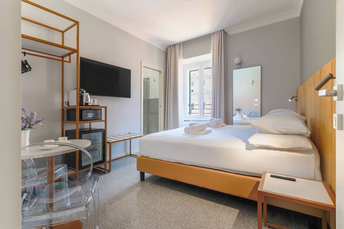 A hotel room with a bed, bedside tables, a TV, a desk with a chair, and a mirror.