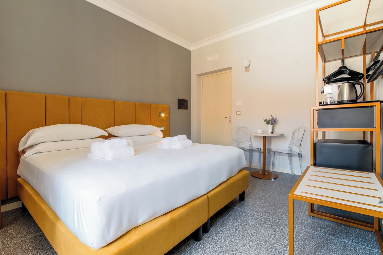 Ein Hotelzimmer mit einem großen Bett, einem kleinen Tisch mit Stühlen und einem Kleiderständer mit Kleiderbügeln.