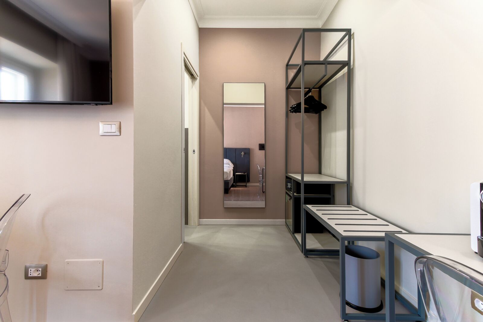 Ett modernt och kompakt hotellrum med en garderob med spegeldörrar, ett litet skrivbord och en papperskorg.