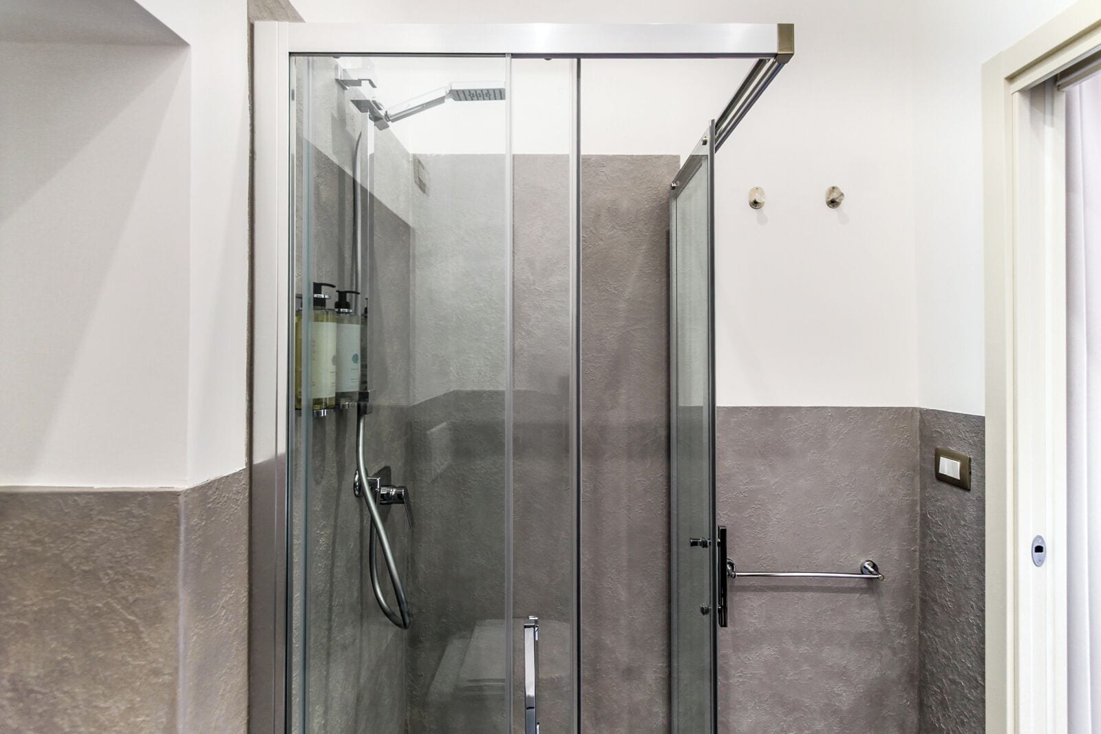 A glass-enclosed shower with a handheld showerhead and a wall-mounted faucet.