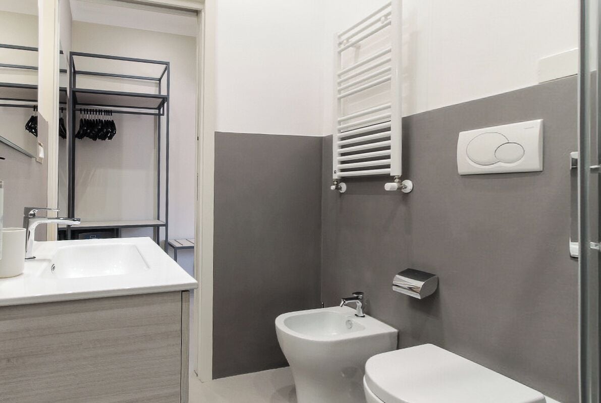 A modern bathroom with a white sink, a bidet, and a toilet. There is a towel rack and a towel warmer on the wall.