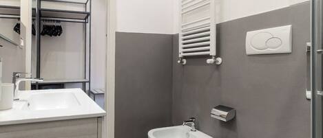 A modern bathroom with a white sink, a bidet, and a toilet. There is a towel rack and a towel warmer on the wall.