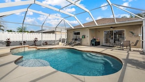 A covered outdoor swimming pool with a patio area, a ceiling fan, and a white fence in the background. - Charming House with Heated Pool (Bradenton)