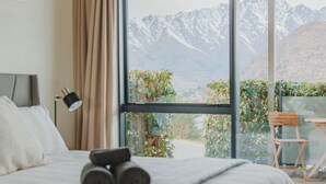Een slaapkamer met een groot bed, uitzicht op bergen en een balkon met een stoel en tafel.