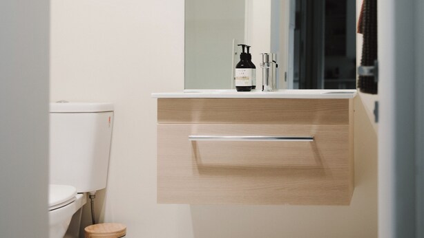 Et moderne badeværelse med toilet, håndvask med spejl og en skraldespand.
