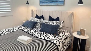 Un dormitorio ordenado con cama, almohadas, una mesita de noche y un cuadro en la pared.