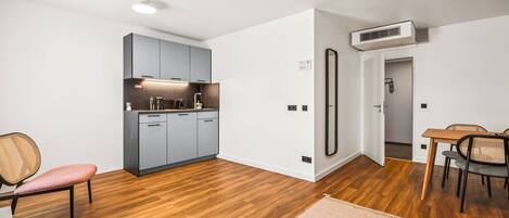 A modern kitchen with grey cabinets, a wooden floor, and a dining area with a table and chairs.
