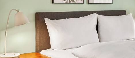 A neatly made bed with white linens, a wooden nightstand with a lamp, and two framed botanical prints on the wall.