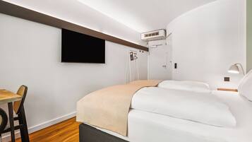 A modern hotel room with a bed, a desk, and a TV mounted on the wall.