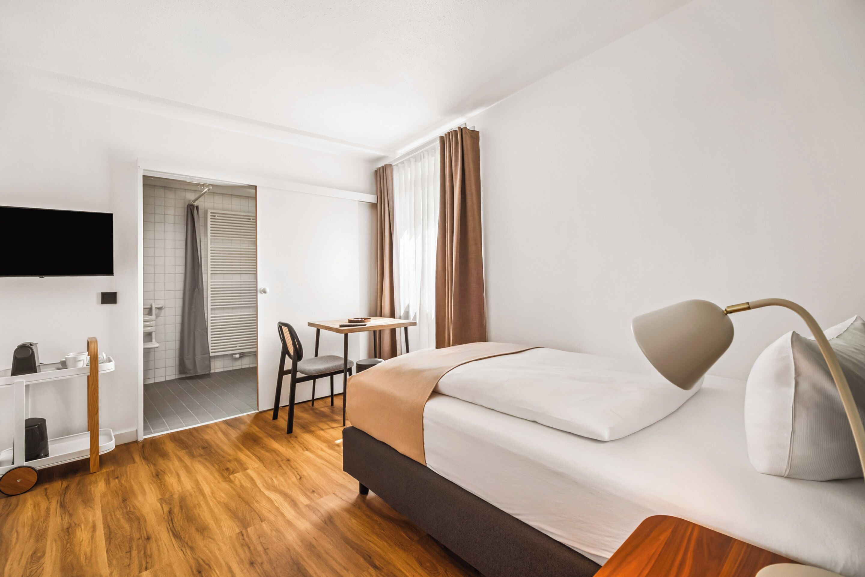 Une chambre d’hôtel avec un lit, un bureau, une chaise, une télévision et une salle de bain visible à travers une porte ouverte.