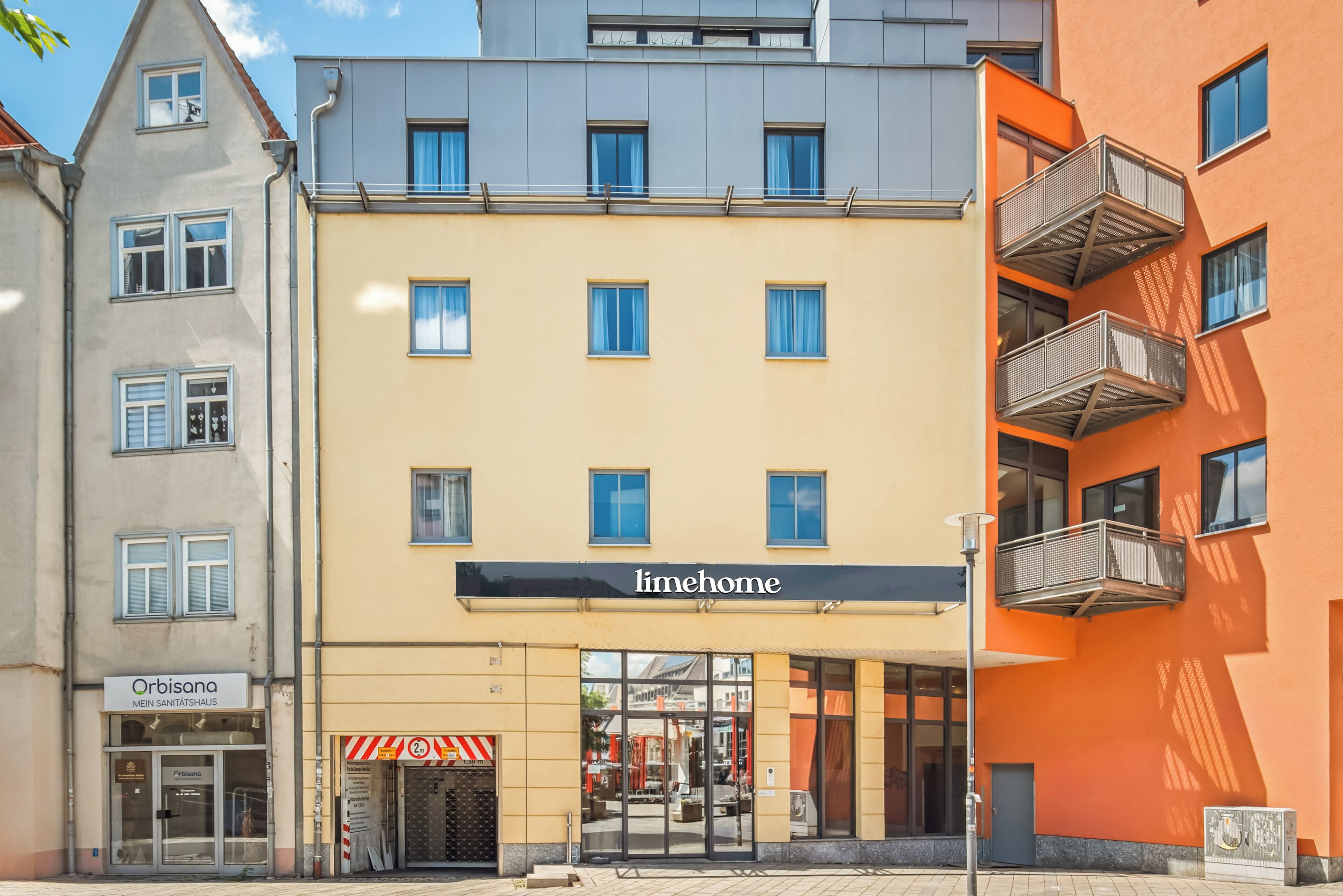 A building with a 'limehome' sign, a 'Mein Santshaus' sign, and a 'Orbisana' sign.