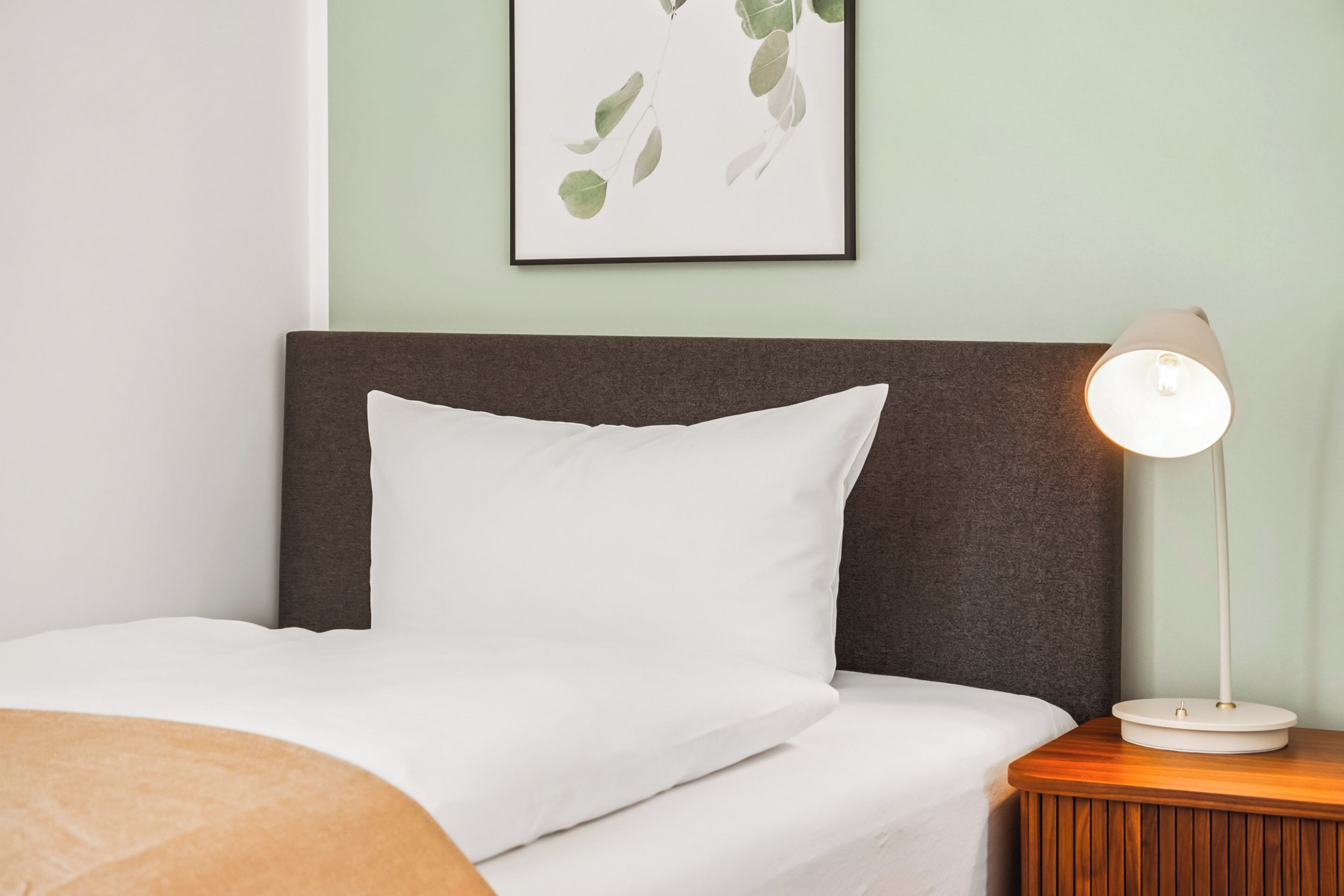 A neatly made bed with white bedding, a dark headboard, and a bedside table with a lamp.