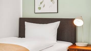 Una cama bien hecha con ropa blanca, un cabecero oscuro y una mesita de noche con una lámpara.