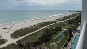 A beach view with a wooden boardwalk, a pool area with lounge chairs, and a pier in the distance. - Amazing views - Kings size Ocean front Camelot 715 (Myrtle Beach)