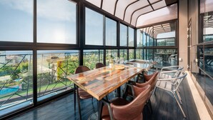 A modern dining area with a wooden table and leather chairs, large windows offering a view of the cityscape and greenery below. - Jigeum Yeosu Ocean View Pension (Yeosu)