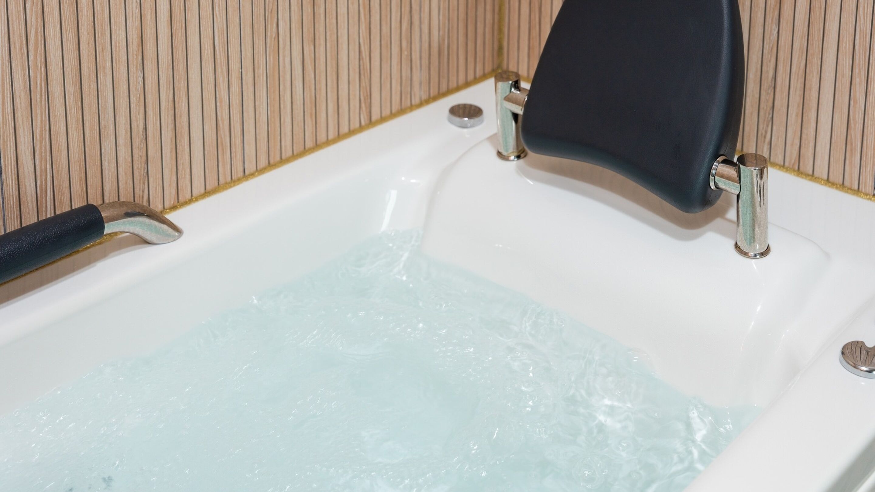 Una bañera con agua corriendo, una toalla negra y un grifo metálico.
