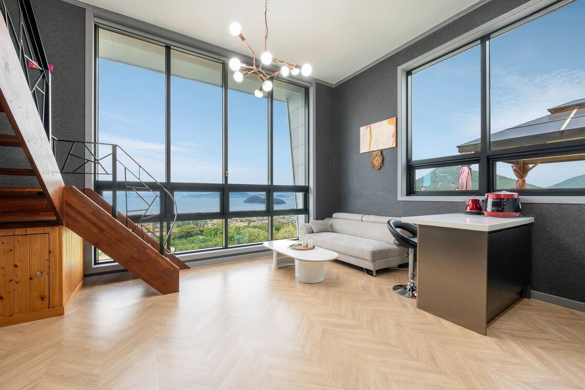 Een ruime woonkamer met een groot raam met uitzicht op de zee, een moderne trap en een gezellige zithoek.