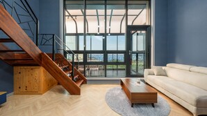 A modern living room with a wooden staircase, a white sofa, and a large window offering a view of the outdoors. - Jigeum Yeosu Ocean View Pension (Yeosu)